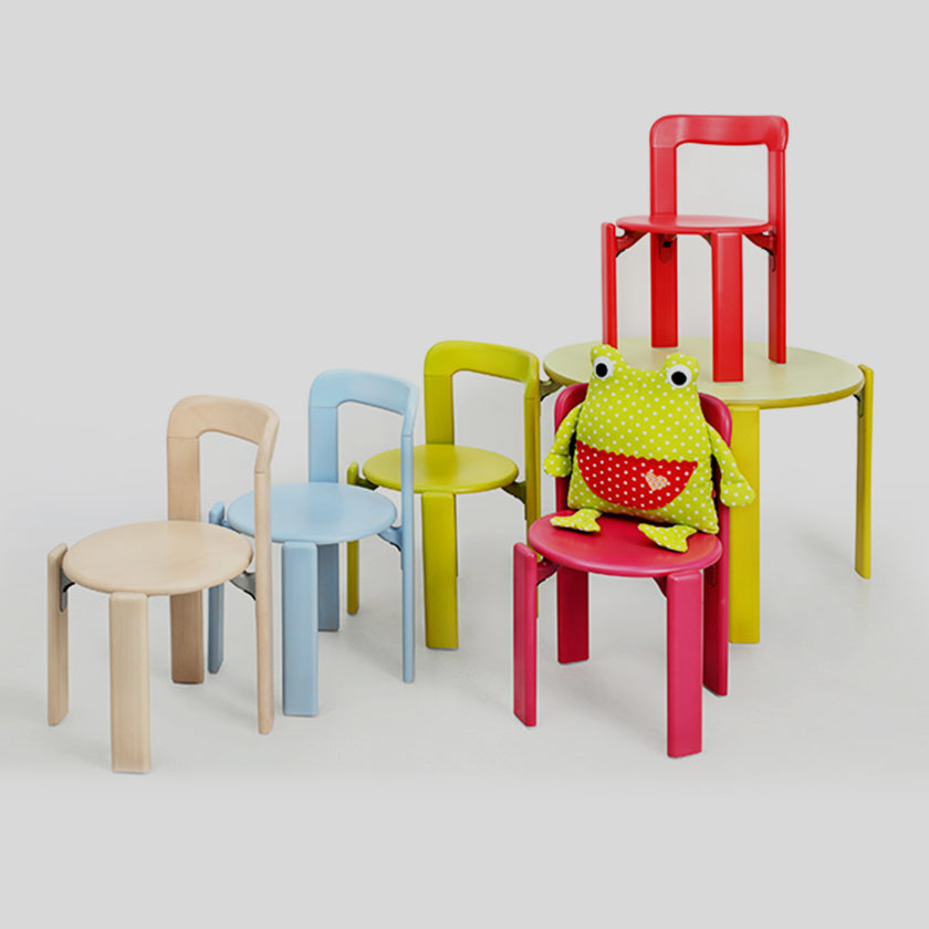 Zusammenstellung von verschiedenfarbigen Kinderstühlen und einem Kuscheltier-Frosch, der auf einem Stuhl sitzt